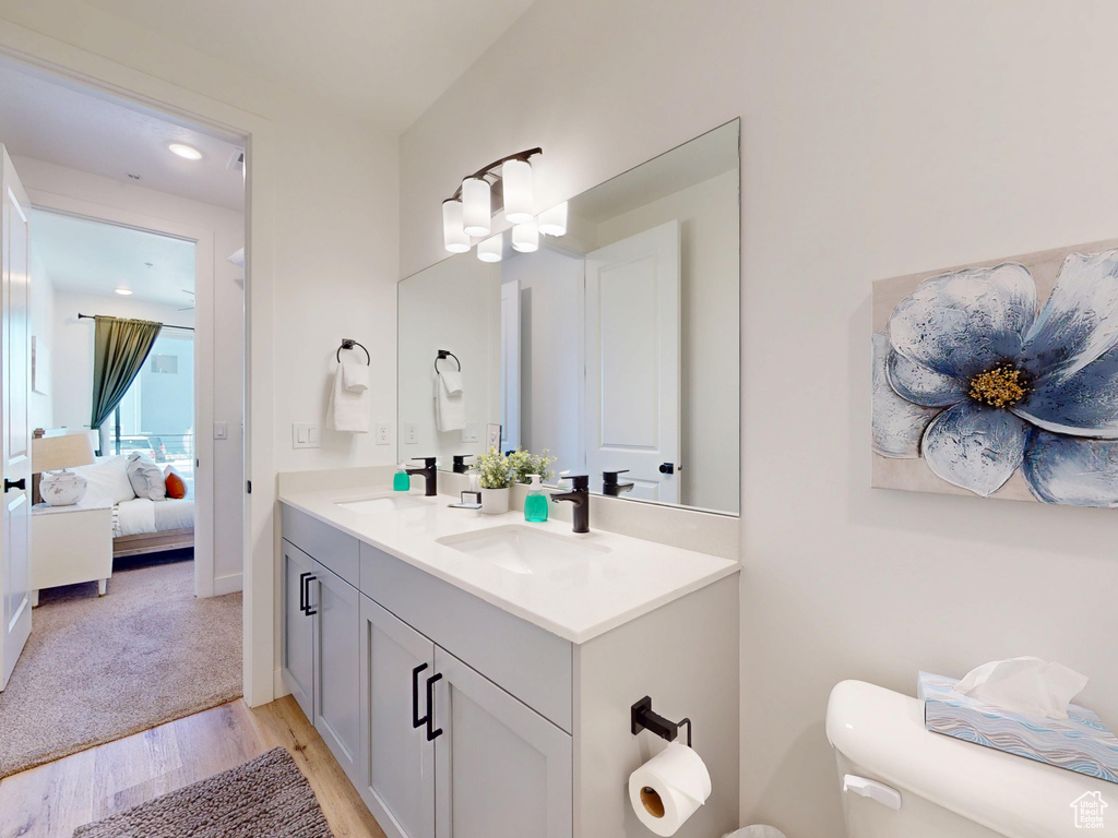 Ensuite bathroom with wood finished floors, connected bathroom, double vanity, toilet, and a sink