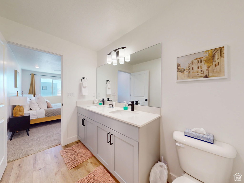 Bathroom with a sink, double vanity, ensuite bathroom, toilet, and wood finished floors
