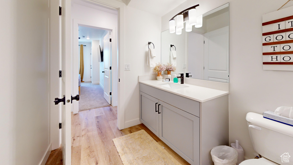 Half bathroom with toilet, wood finished floors, vanity, and baseboards