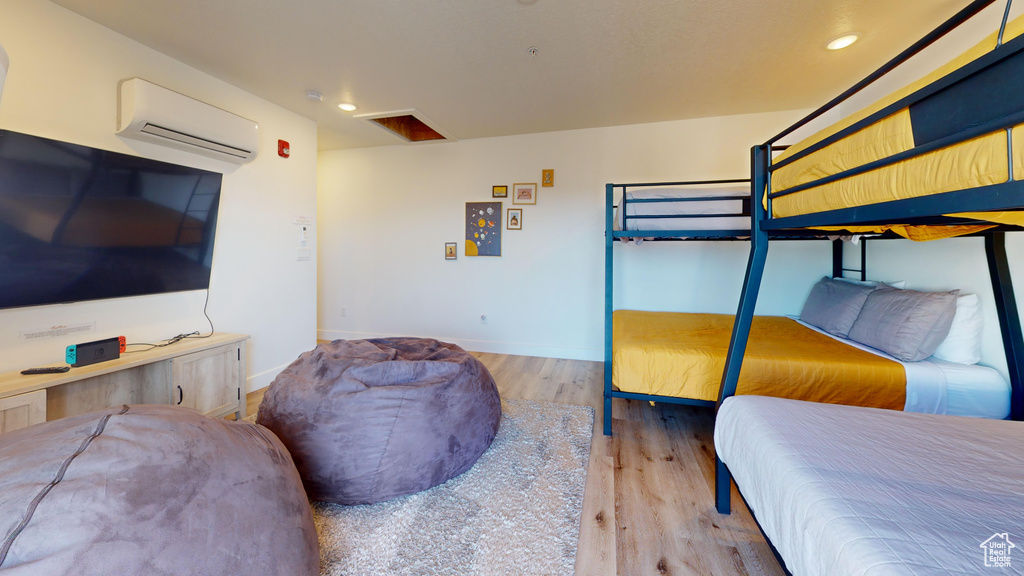 Bedroom with wood finished floors, a wall mounted air conditioner, recessed lighting, and baseboards