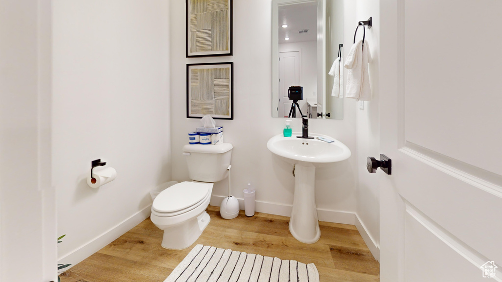 Half bathroom with toilet, wood finished floors, and baseboards