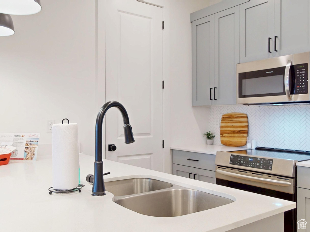 Kitchen with decorative backsplash, stainless steel appliances, light countertops, a sink, and gray cabinetry
