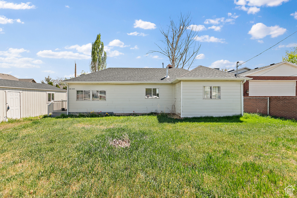 Back of property featuring fence, roof with shingles, and a lawn