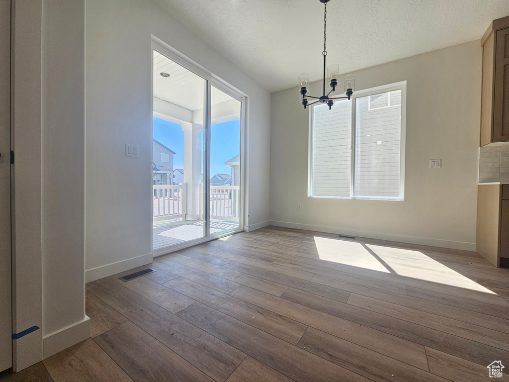 Unfurnished dining area with a chandelier, wood-type flooring, and baseboards