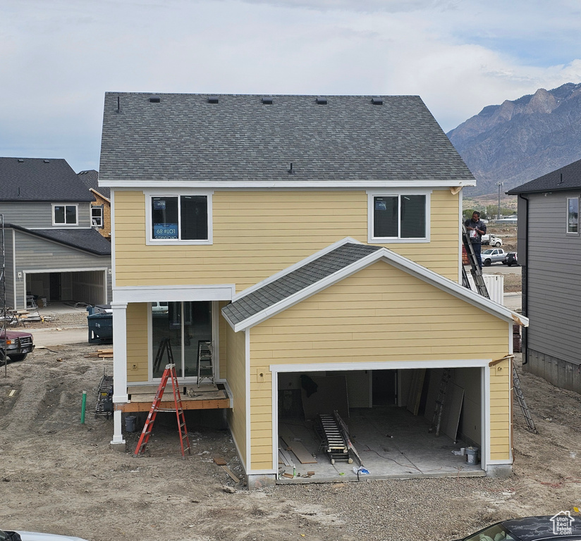 Rear view of house featuring a mountain view, driveway, a garage, and a shingled roof