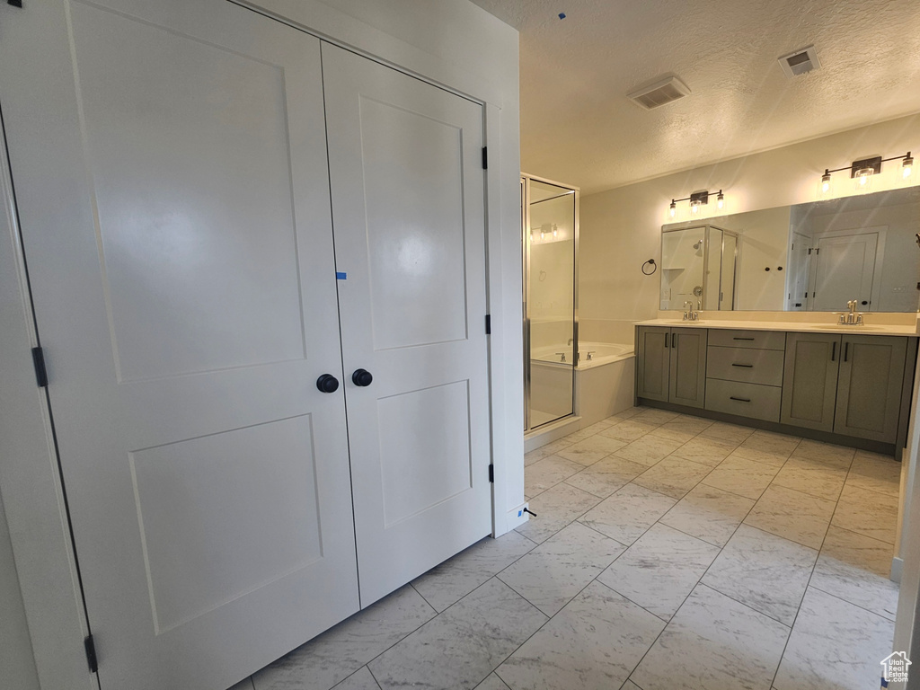 Bathroom featuring marble look tiles, double vanity, a textured ceiling, a shower stall, and a garden tub