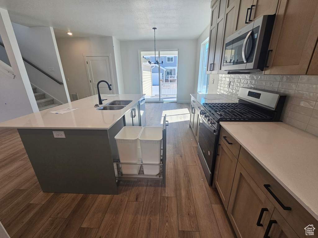 Kitchen featuring a sink, stainless steel appliances, dark wood-style floors, an island with sink, and tasteful backsplash