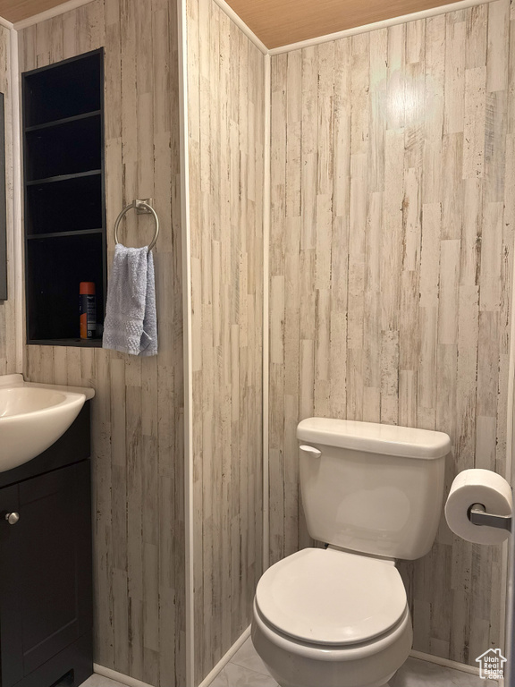 Half bath with baseboards, wooden walls, toilet, and vanity