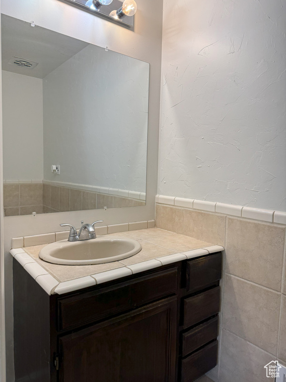 Bathroom with tile walls, visible vents, wainscoting, and vanity