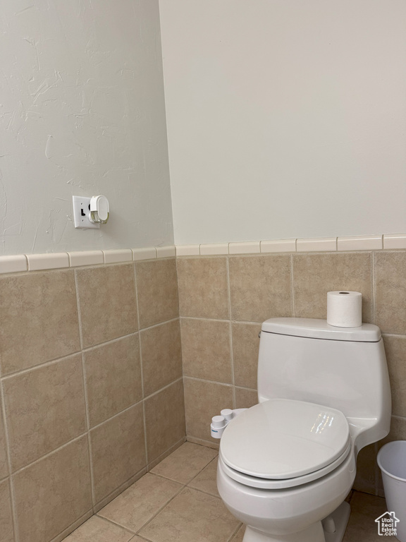 Bathroom with tile patterned floors, toilet, a wainscoted wall, and tile walls