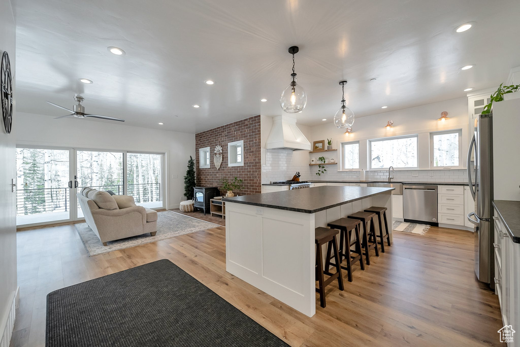 Kitchen featuring a wood stove, dark countertops, stainless steel appliances, premium range hood, and a kitchen bar