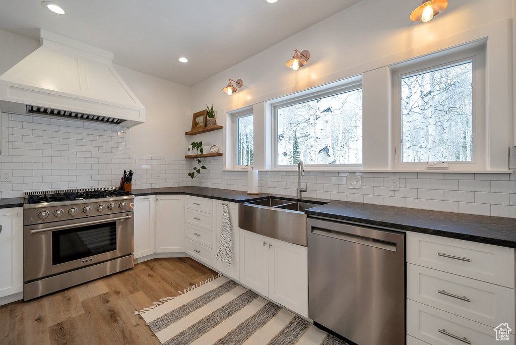 Kitchen with dark countertops, custom exhaust hood, stainless steel appliances, and a sink