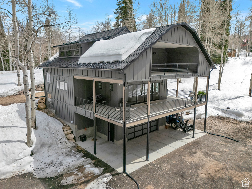 Snow covered rear of property with roof with shingles, board and batten siding, and a balcony