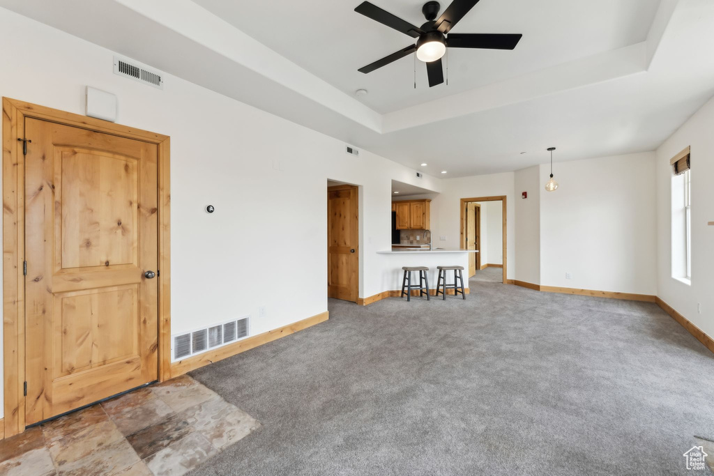 Unfurnished living room featuring baseboards, visible vents, ceiling fan, and a tray ceiling