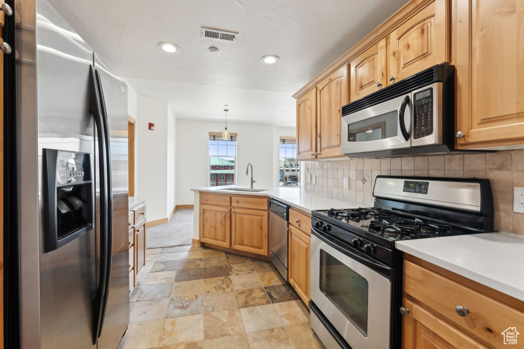 Kitchen featuring tasteful backsplash, stone finish floor, appliances with stainless steel finishes, a sink, and a peninsula