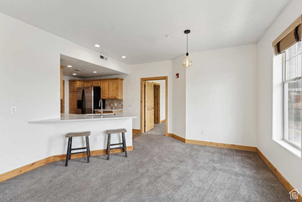 Kitchen featuring a sink, light countertops, stainless steel refrigerator with ice dispenser, baseboards, and light colored carpet