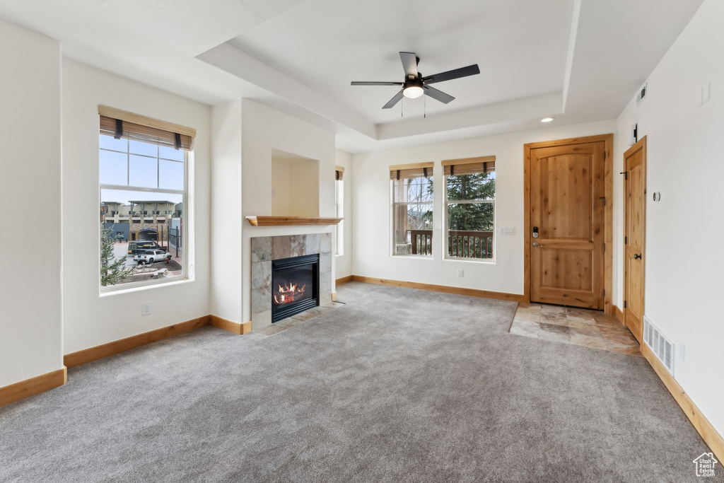 Unfurnished living room featuring a raised ceiling, a wealth of natural light, and carpet floors