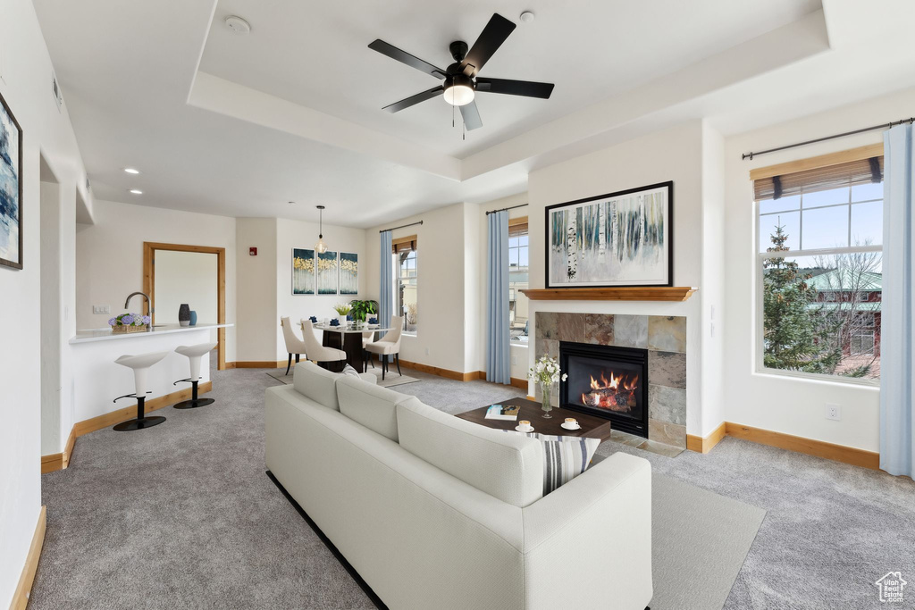 Carpeted living area featuring a fireplace, baseboards, recessed lighting, a tray ceiling, and a ceiling fan