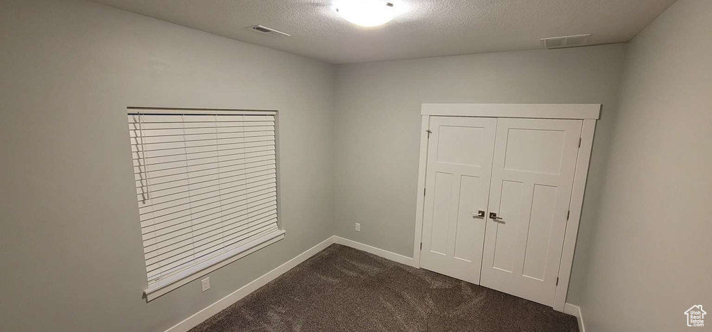 Unfurnished bedroom featuring baseboards, dark carpet, a textured ceiling, and visible vents