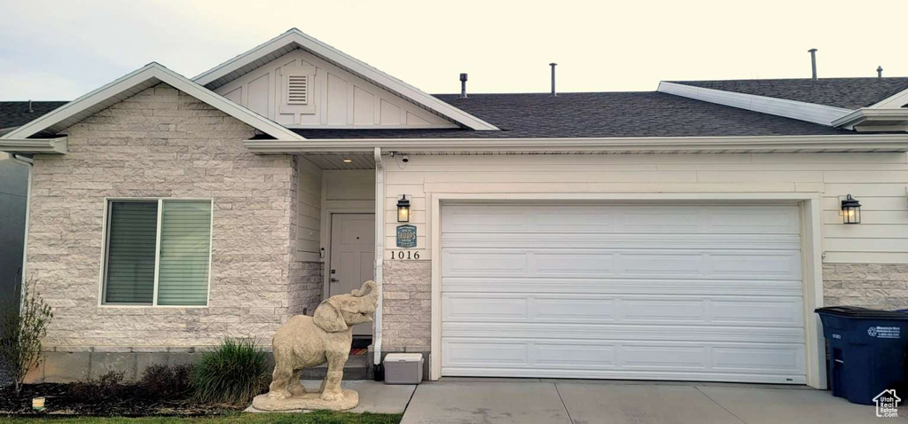 View of front of house featuring board and batten siding, roof with shingles, concrete driveway, an attached garage, and stone siding