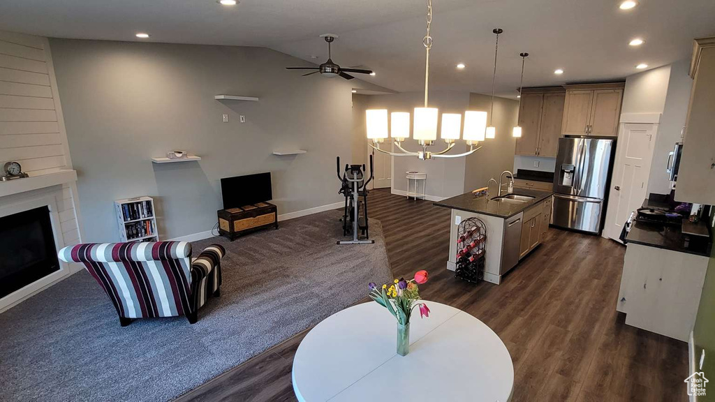 Living area with a fireplace, ceiling fan with notable chandelier, recessed lighting, vaulted ceiling, and dark wood-style floors