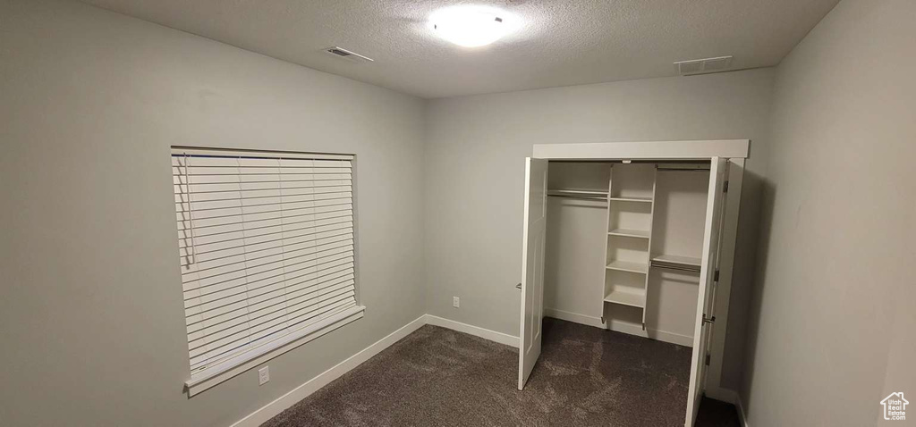 Unfurnished bedroom with a textured ceiling, dark colored carpet, baseboards, visible vents, and a closet