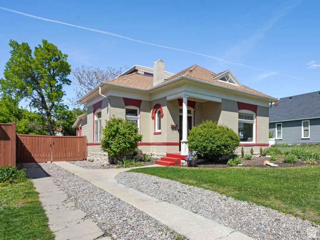 Bungalow-style house featuring a front lawn, covered porch, driveway, a chimney, and fence