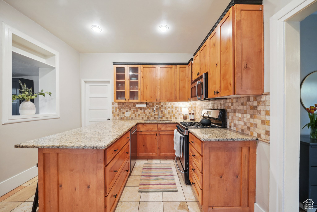 Kitchen with light stone countertops, appliances with stainless steel finishes, backsplash, a sink, and a peninsula