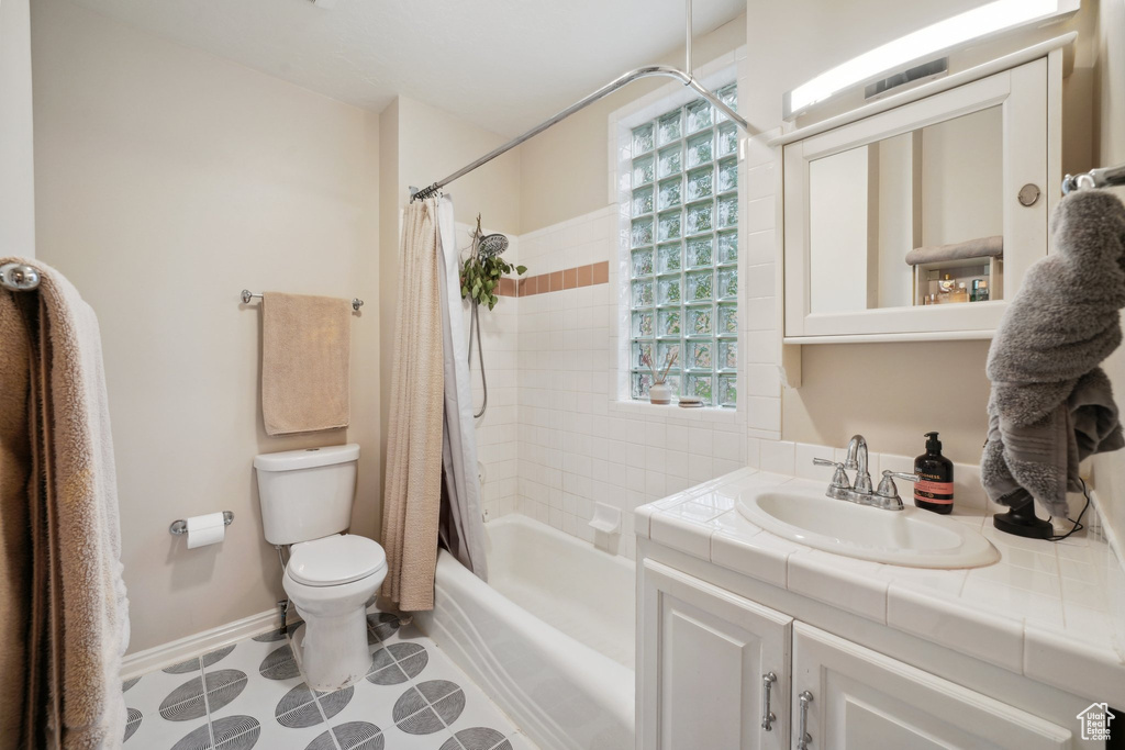 Bathroom featuring toilet, shower / bath combination with curtain, vanity, and baseboards