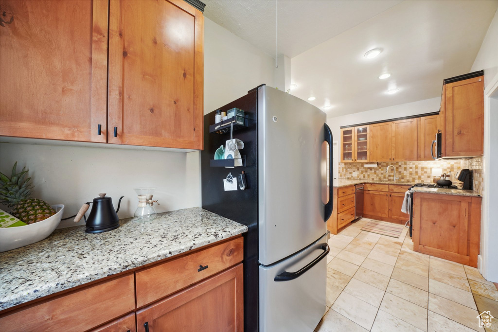Kitchen with brown cabinets, light stone counters, stainless steel appliances, and tasteful backsplash