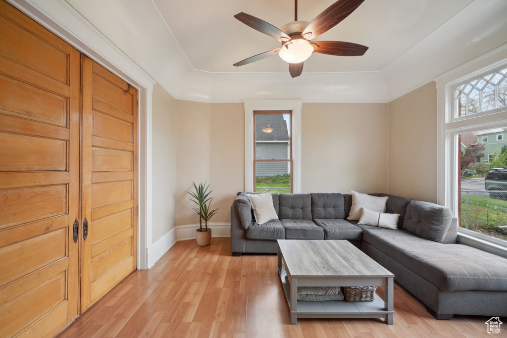 Living area with ceiling fan, a wealth of natural light, a raised ceiling, and light wood-type flooring