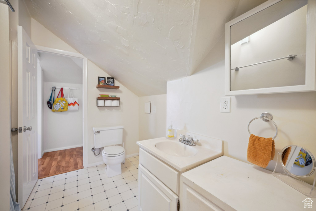 Bathroom featuring baseboards, toilet, vaulted ceiling, tile patterned floors, and vanity