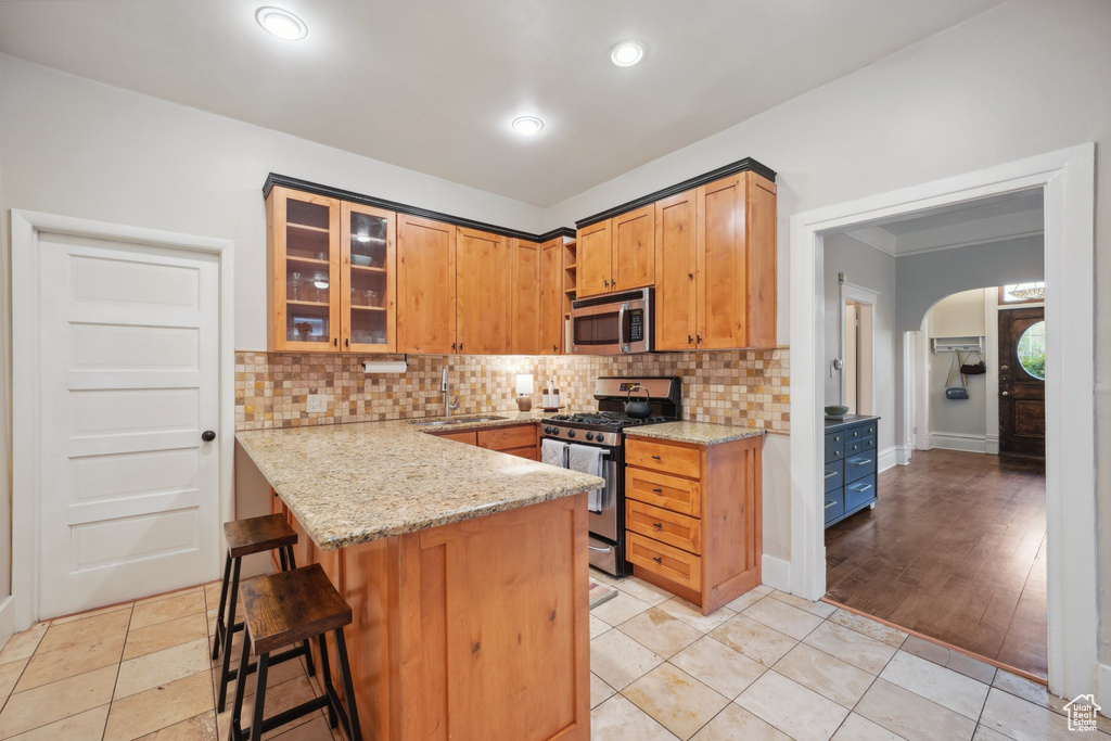 Kitchen with a sink, backsplash, light stone counters, arched walkways, and appliances with stainless steel finishes