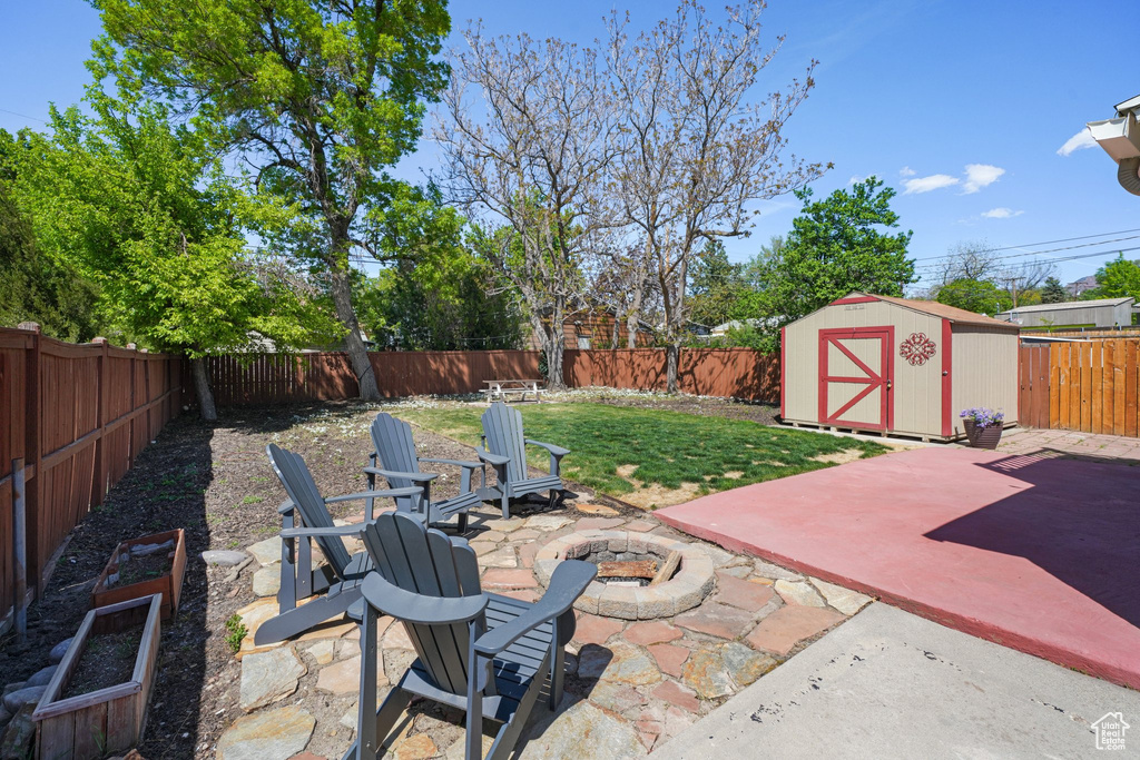 View of patio with an outbuilding, a storage shed, a fenced backyard, and an outdoor fire pit