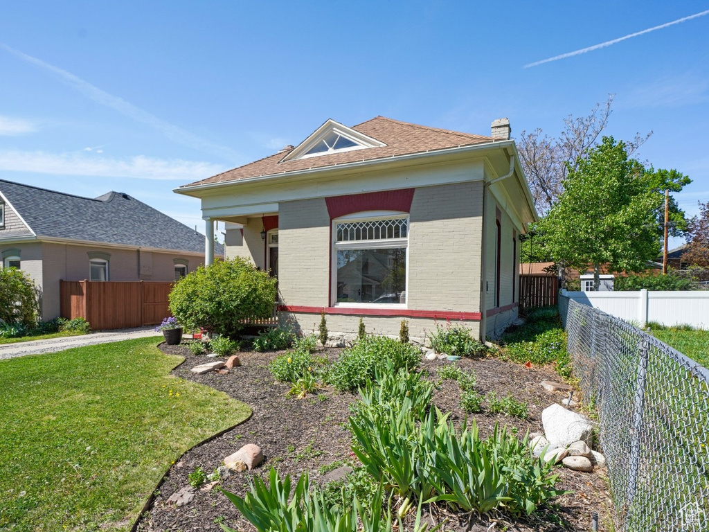 Bungalow with a chimney, brick siding, fence, and a front yard
