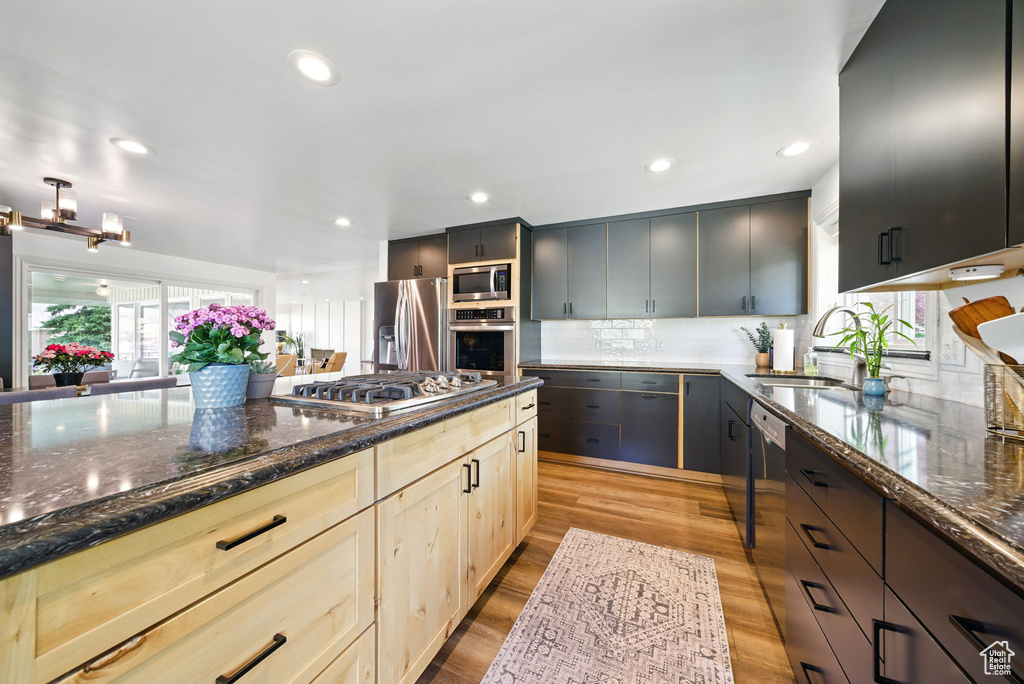 Kitchen featuring appliances with stainless steel finishes, a sink, light wood-style floors, dark stone counters, and backsplash