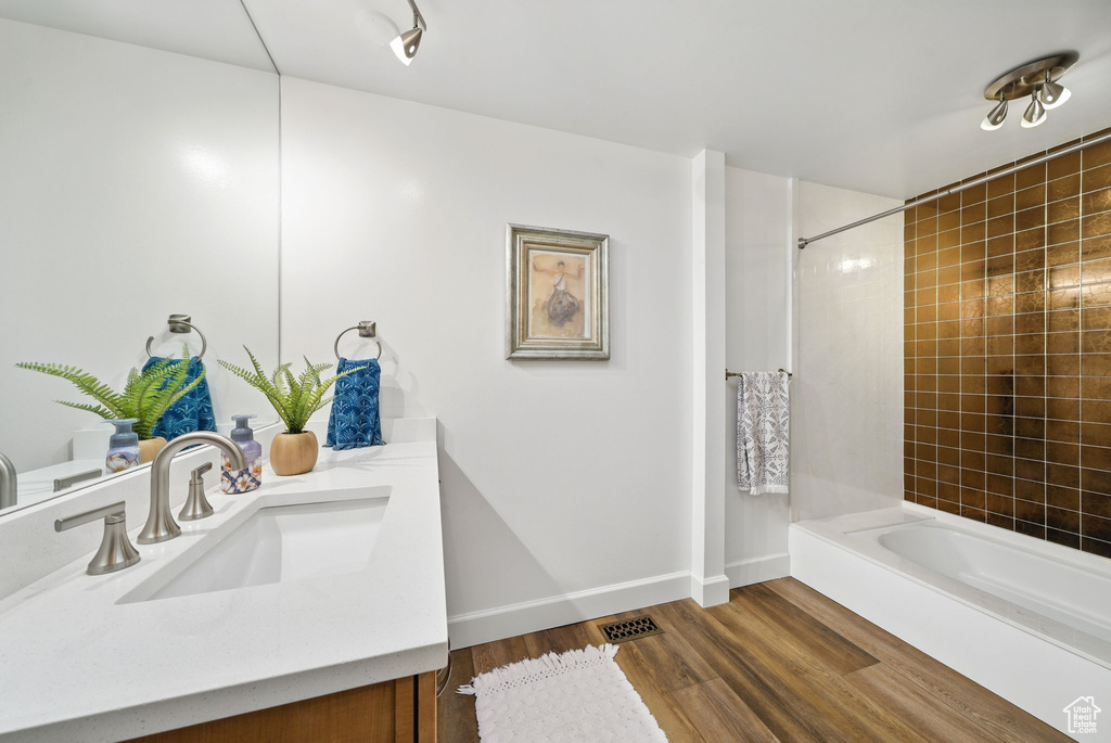 Full bath with vanity, baseboards, wood finished floors,  shower combination, and visible vents