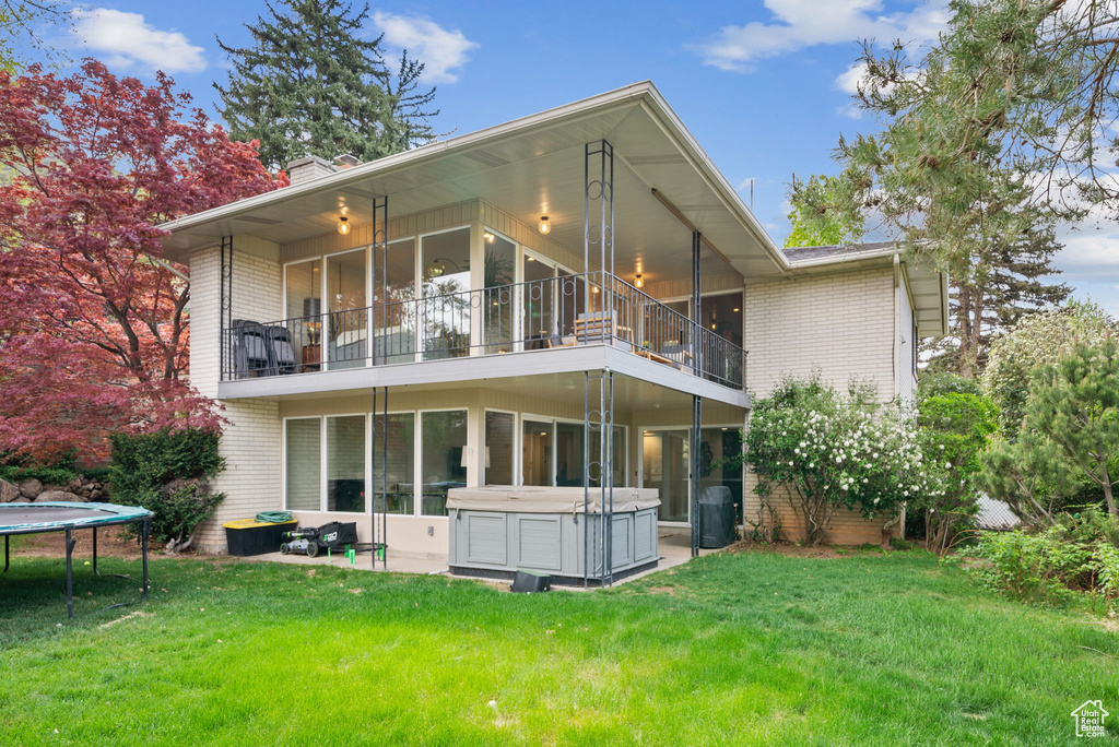 Back of house featuring a balcony, a trampoline, a hot tub, and brick siding