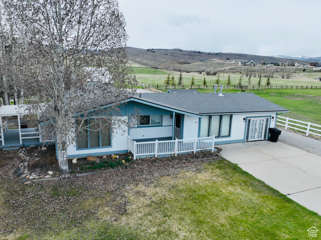 Ranch-style home with fence, roof with shingles, a front lawn, concrete driveway, and a rural view