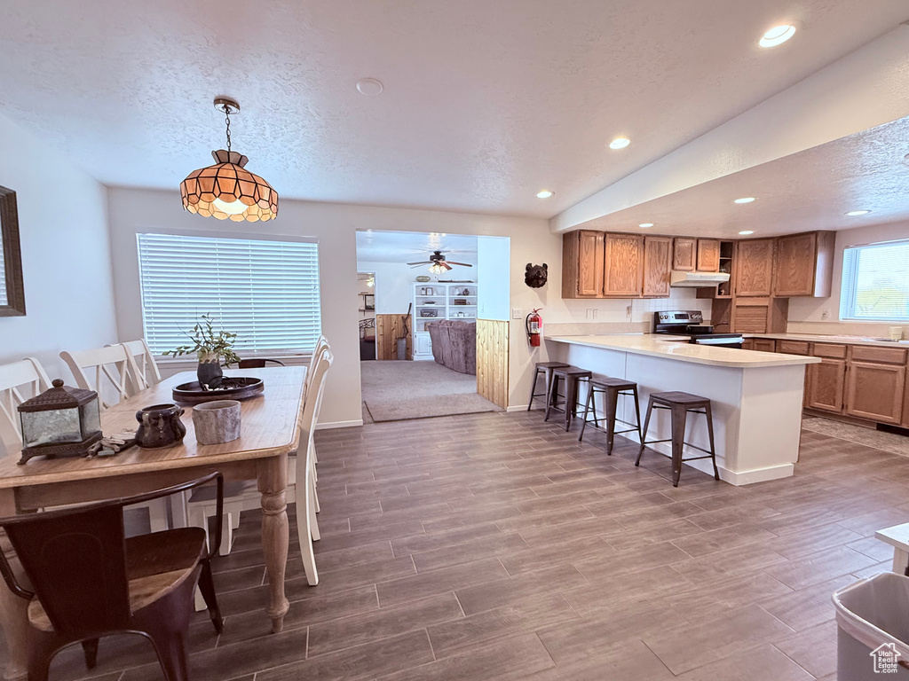 Kitchen with a kitchen breakfast bar, ceiling fan, stainless steel range with electric stovetop, a peninsula, and under cabinet range hood