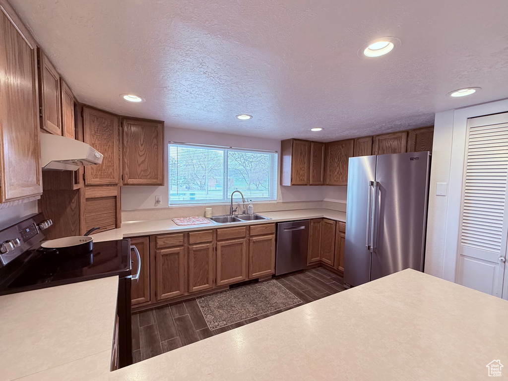 Kitchen featuring wood tiled floor, recessed lighting, under cabinet range hood, a sink, and appliances with stainless steel finishes