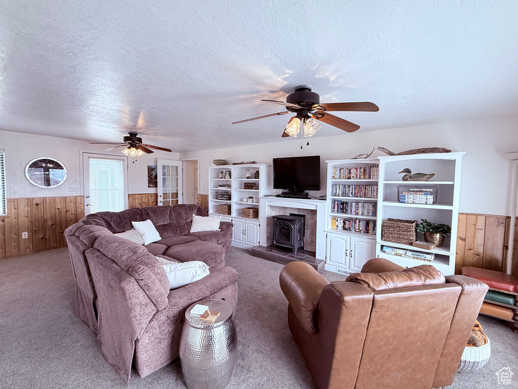 Carpeted living room featuring a wood stove, wainscoting, ceiling fan, and wooden walls