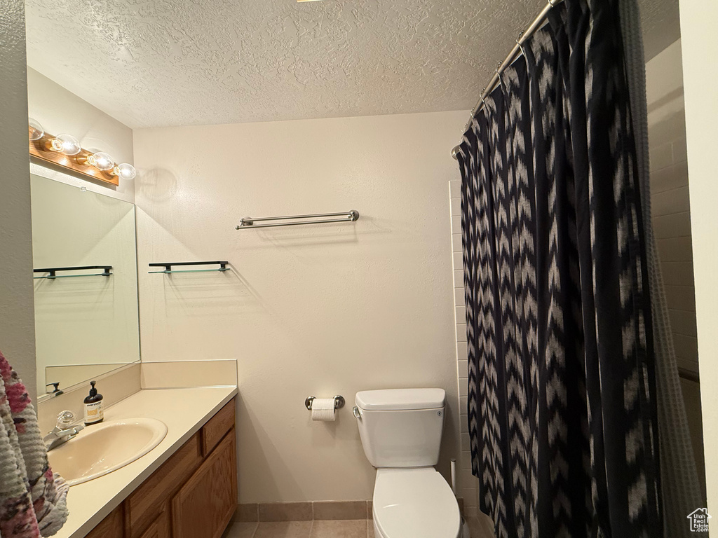Bathroom with vanity, toilet, a textured ceiling, tile patterned floors, and a shower with curtain