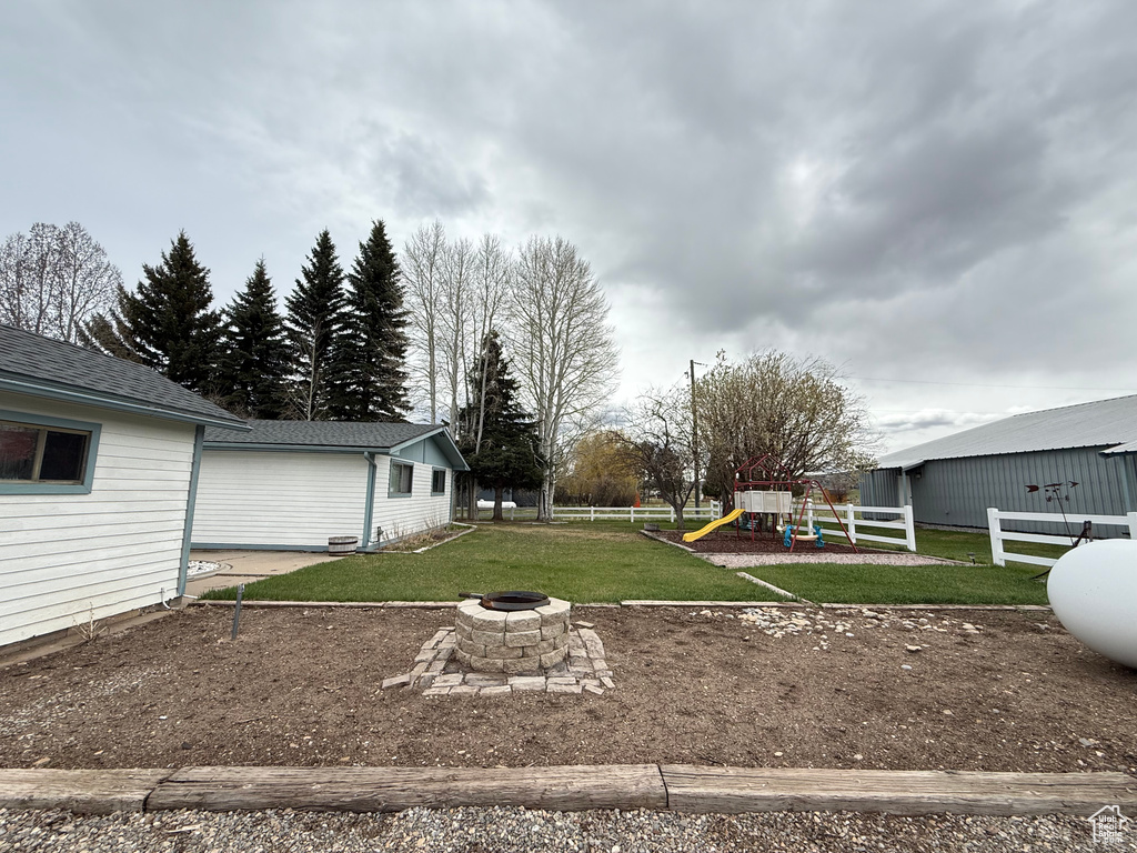 View of yard with fence, a playground, and an outdoor fire pit