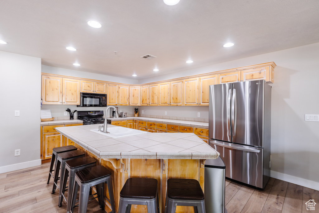 Kitchen with visible vents, light brown cabinetry, baseboards, light wood-type flooring, and black appliances