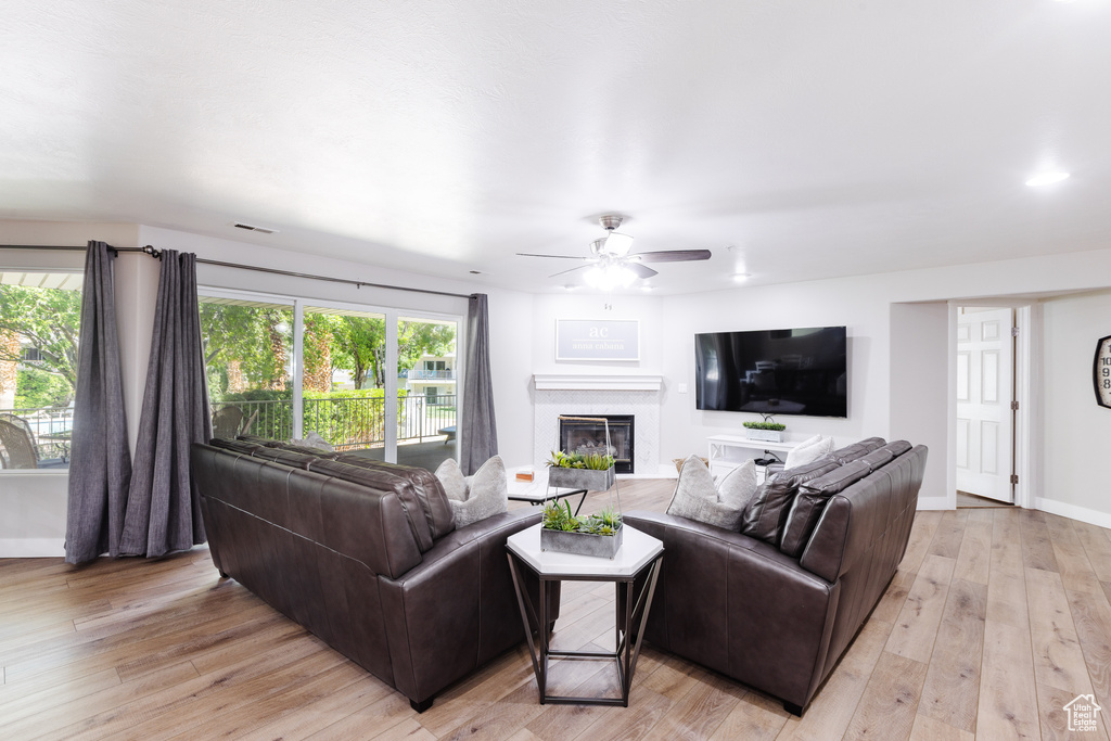Living room with light wood-style floors, a ceiling fan, visible vents, baseboards, and a glass covered fireplace