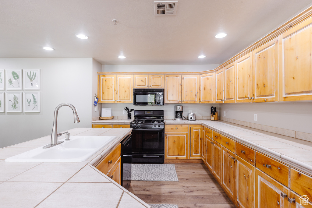 Kitchen featuring tile countertops, visible vents, a sink, black appliances, and light wood-style floors