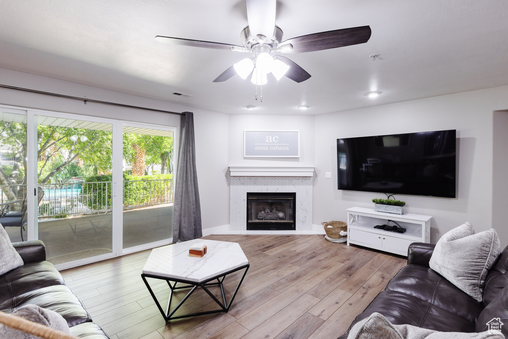 Living area with ceiling fan, a fireplace, baseboards, wood finished floors, and visible vents