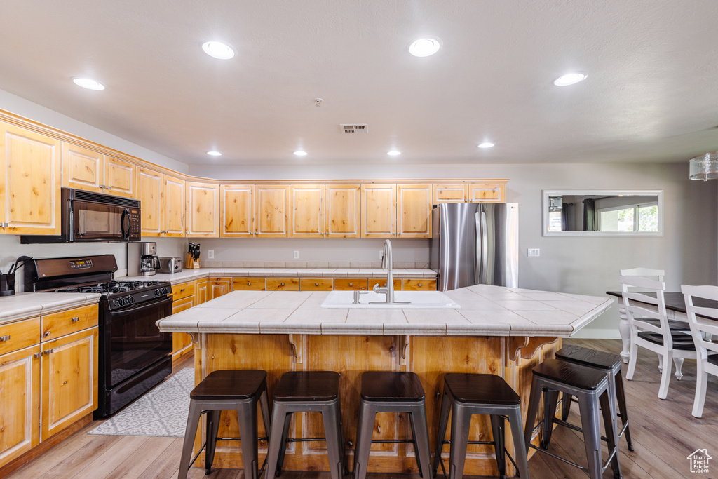 Kitchen with visible vents, tile countertops, a sink, light wood-style flooring, and black appliances