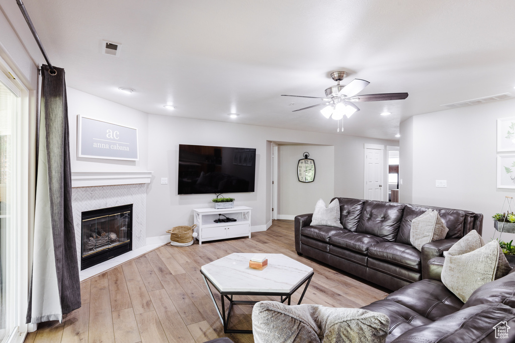 Living room with a glass covered fireplace, a ceiling fan, wood finished floors, and visible vents